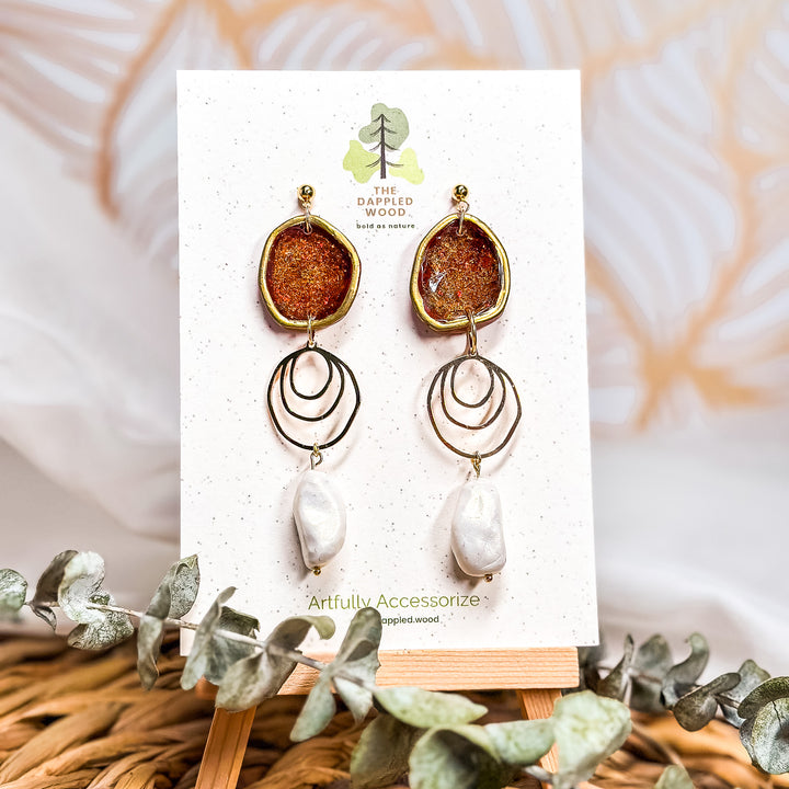 The Dappled Wood Fall 2025 Rhea earrings in brick red with faux baroque pearls, displayed on a branded earring card, styled as a statement accessory for fall outfits, autumn gatherings, and Thanksgiving jewelry looks.