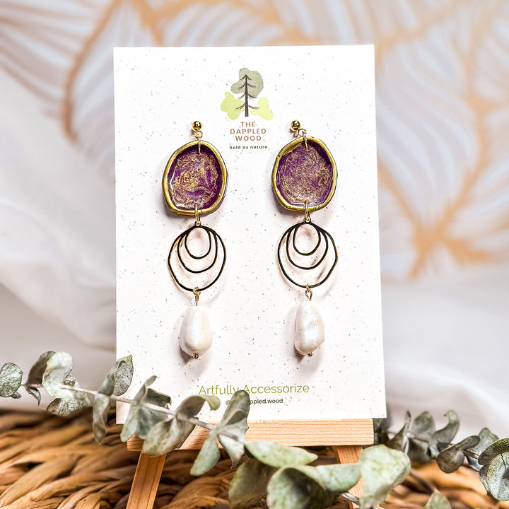 The Dappled Wood Fall 2025 Rhea earrings in dark plum with faux baroque pearls, displayed on a branded earring card, styled as a bold statement accessory for fall outfits, autumn gatherings, and Thanksgiving looks.
