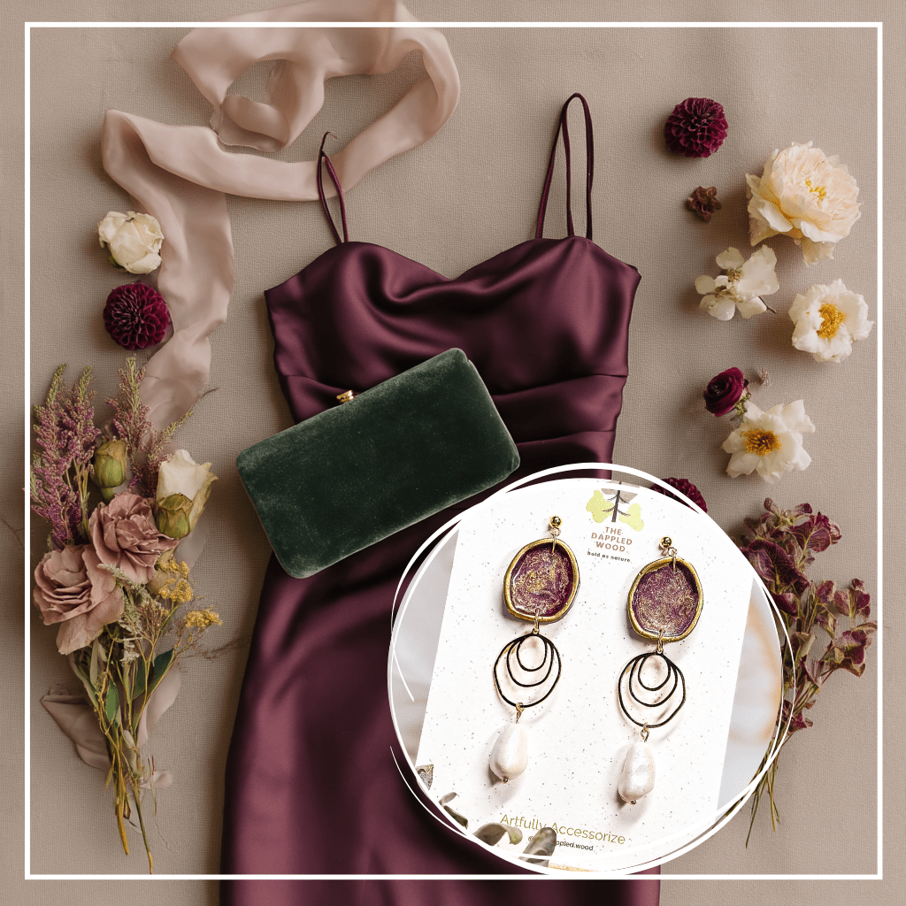 The Dappled Wood Fall 2025 Rhea earrings in dark plum with faux baroque pearls, styled with a satin dress, clutch, and florals in a flatlay, designed as statement jewelry for fall wedding guest outfits and autumn celebrations.