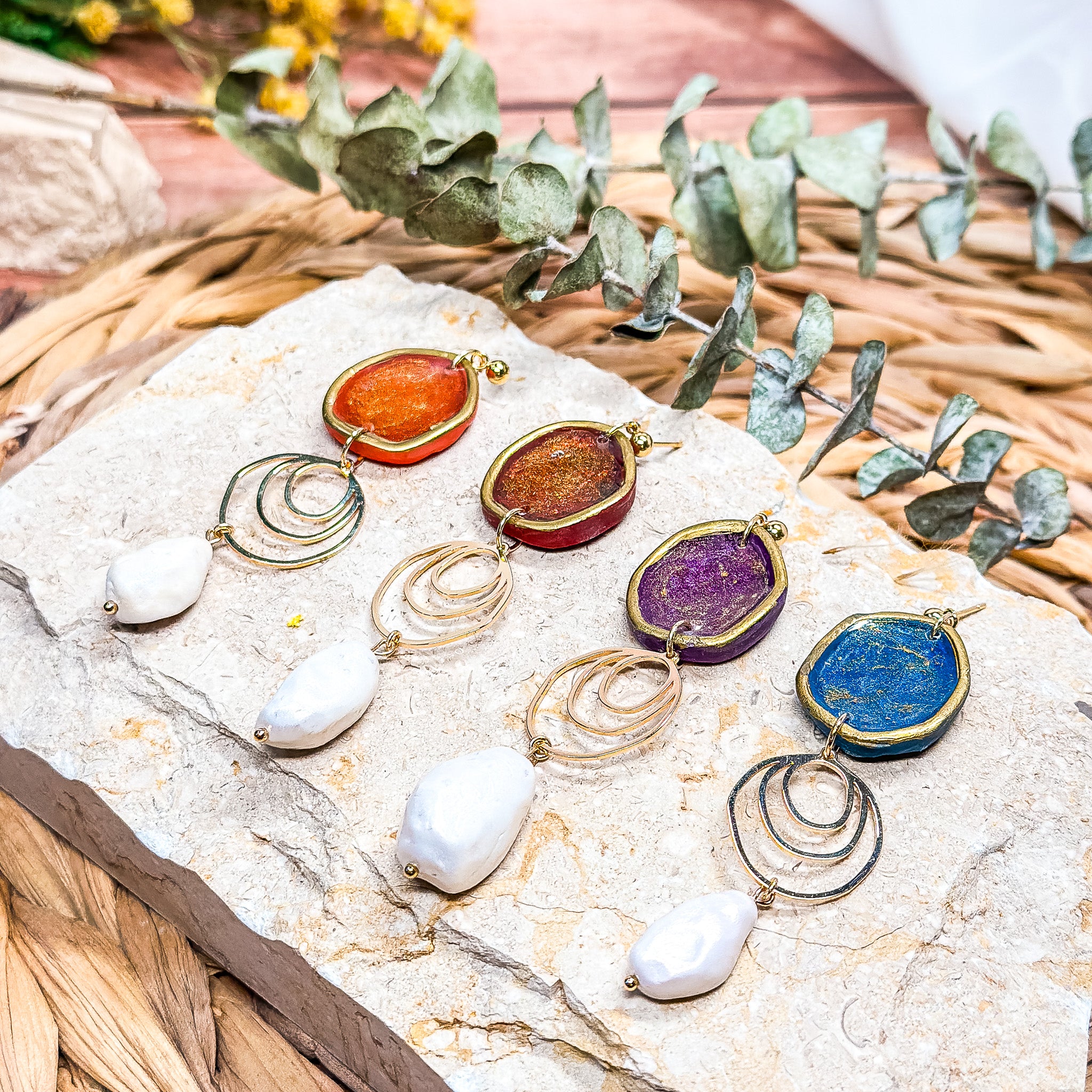 The Dappled Wood Fall 2025 Rhea earrings collection featuring four color variants—pumpkin orange, brick red, dark plum, and navy blue—with faux baroque pearls, displayed on a stone surface as statement jewelry for fall outfits, autumn gatherings, and Thanksgiving looks.