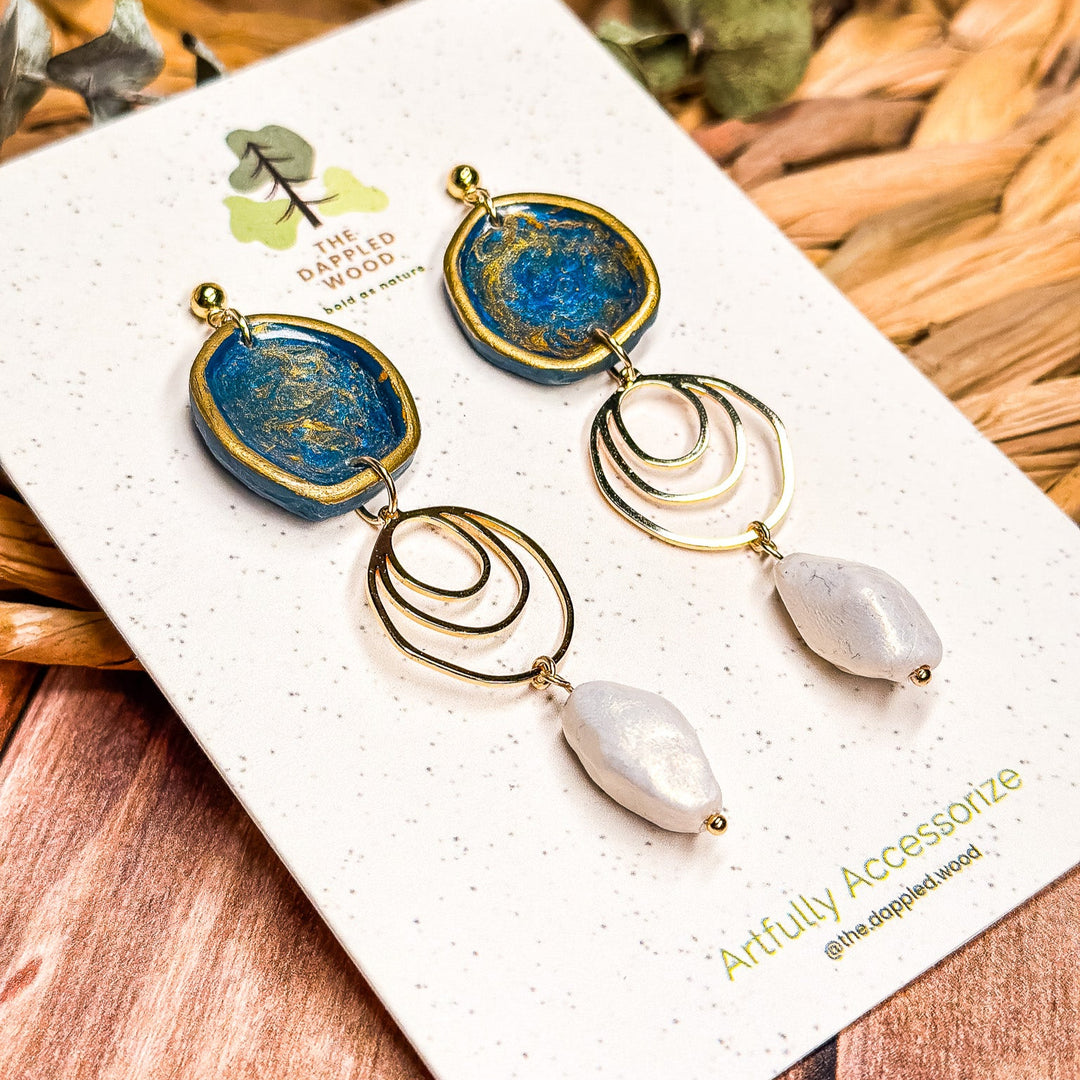 The Dappled Wood Fall 2025 Rhea earrings in navy blue with faux baroque pearls, displayed on a branded earring card, styled as a statement accessory for fall outfits, autumn gatherings, and Thanksgiving looks.