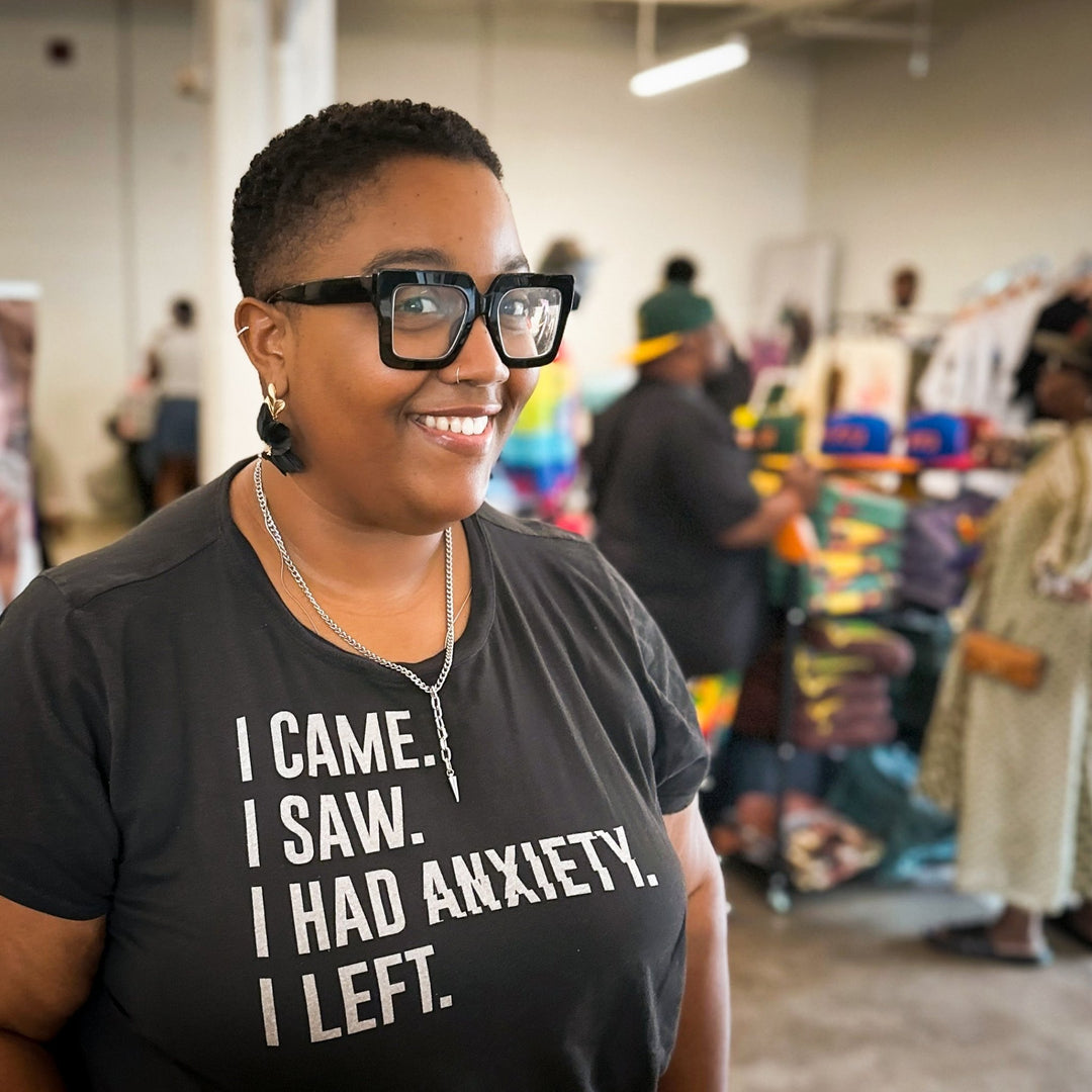 A customer at a local market wearing The Dappled Wood Flora earrings in black, showing the bold lightweight statement jewelry in a real life setting with other vendors in the background.