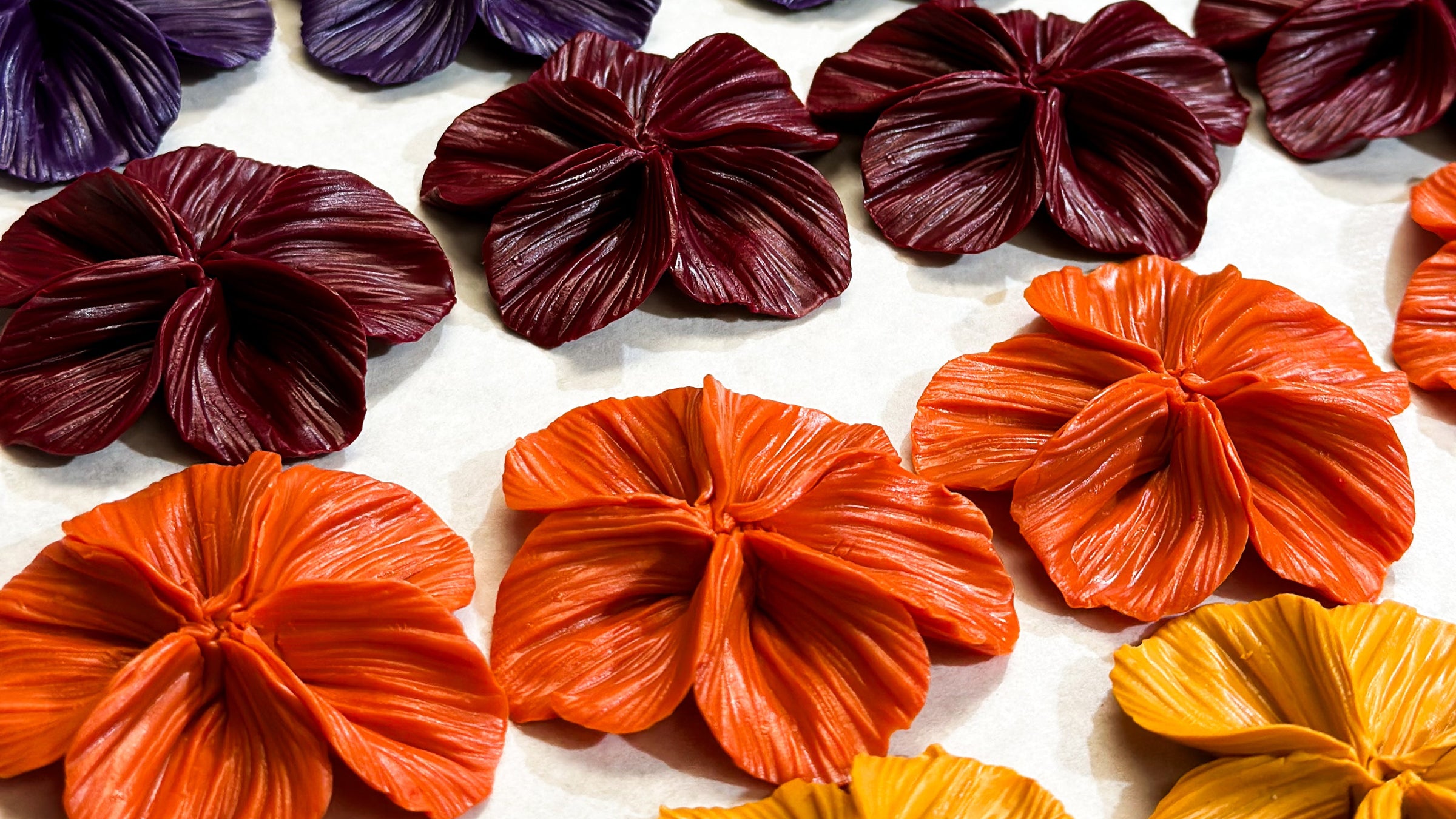 Unfinished Flora earrings by The Dappled Wood displayed in rich fall colors, showcasing handcrafted petal details in deep burgundy, orange, and gold for a seasonal collection preview.