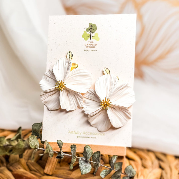 The Dappled Wood's Flora handmade flower earrings in white with gold findings displayed on a branded earring cards. 