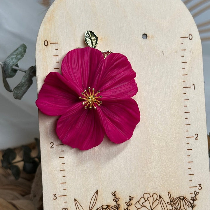 The Dappled Wood Flora earring in fuchsia displayed on a measurement board to show the size and detailed petals of this lightweight statement jewelry piece.