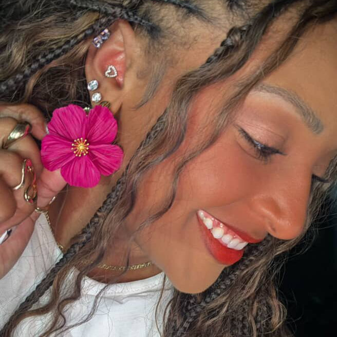 The Dappled Wood Flora earrings in fuchsia worn by a smiling customer, showing the bold petal detail and lightweight statement style.