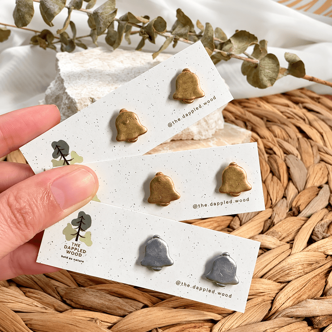 Gladys handmade Christmas bell stud earrings in gold and silver finishes on display cards.