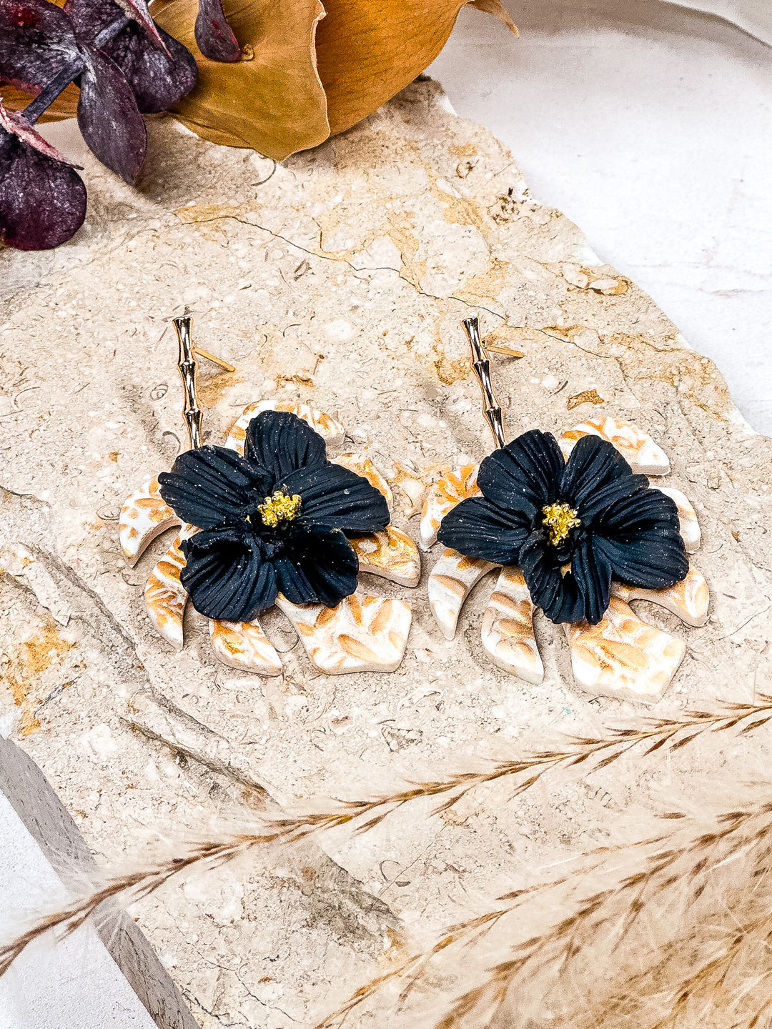 White monstera earrings with gold embossed detailing and a black flower accent, hypoallergenic jewelry by The Dappled Wood.