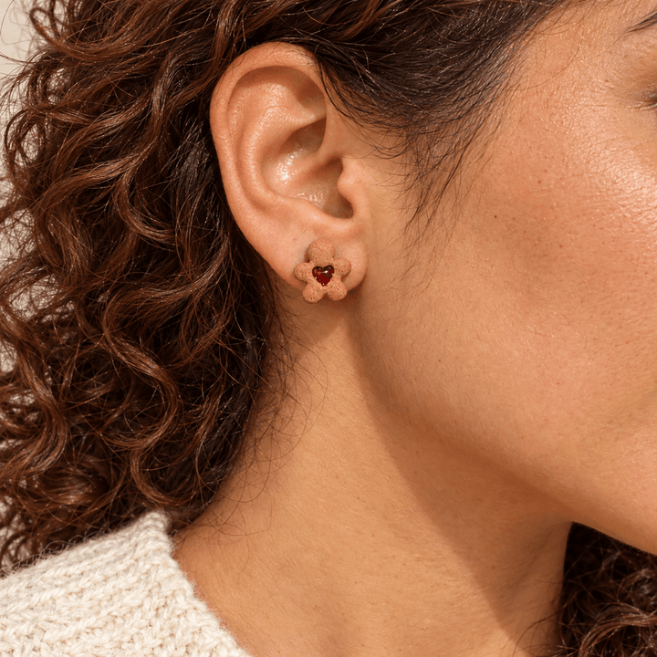 AI-generated styling preview of Greta stud earrings on a model with natural brown hair; scale illustrative.