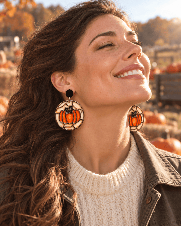 Smiling woman wearing Hazel stained glass pumpkin earrings at a sunlit pumpkin patch.