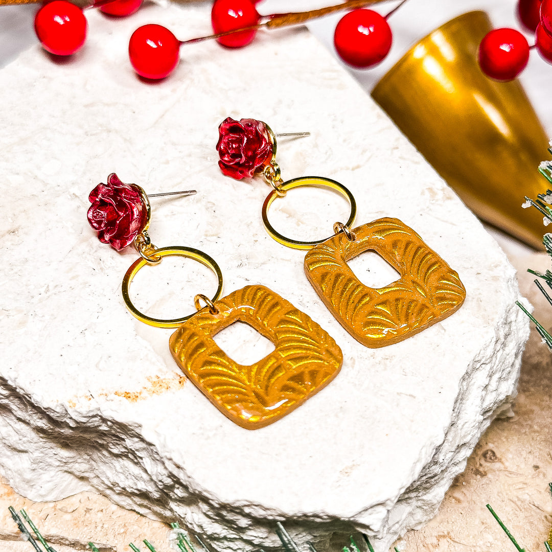 The Dappled Wood Belle earrings in a flat lay setting with a festive backdrop, showcasing gold geometric dangles and delicate floral accents. Handmade, hypoallergenic holiday jewelry.