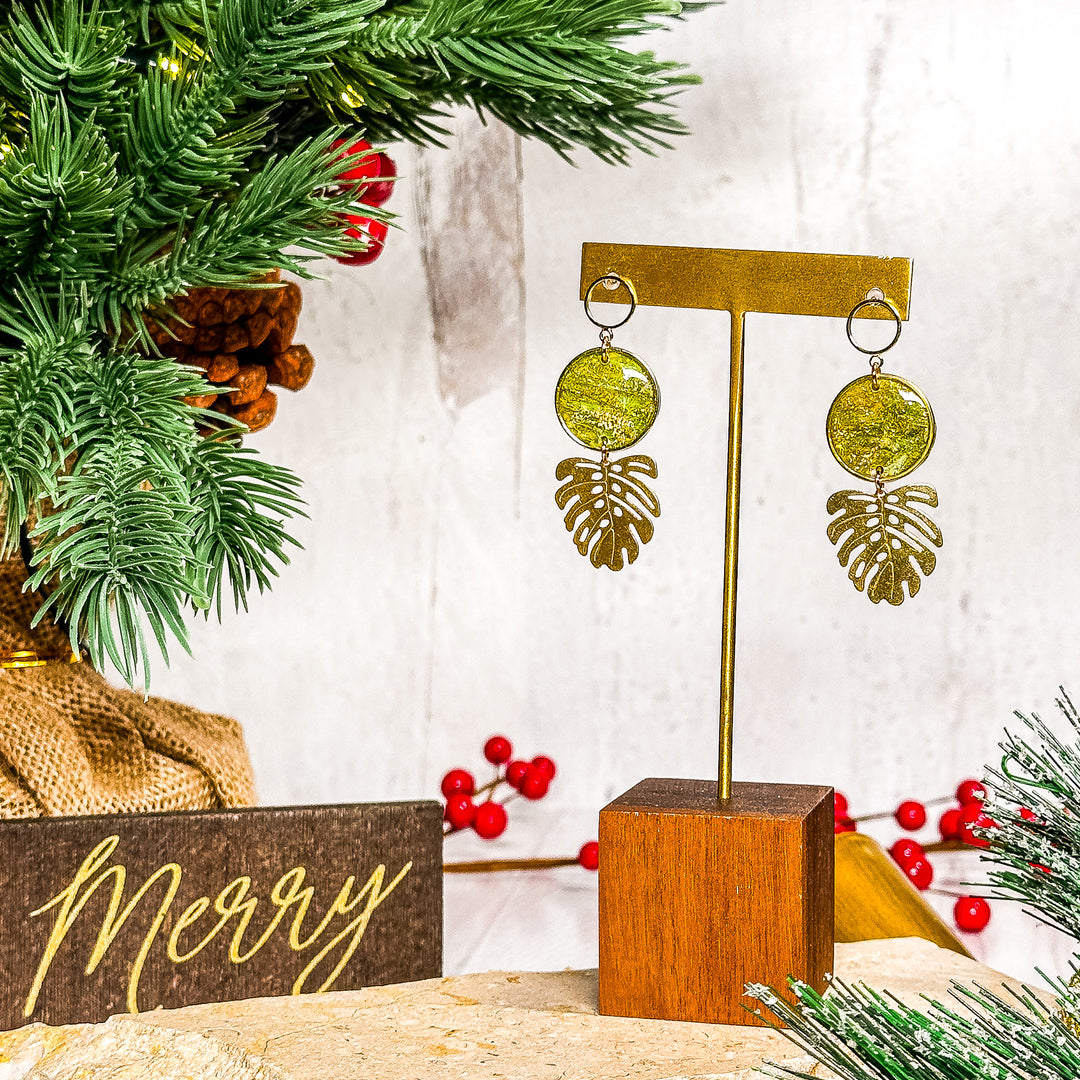 The Dappled Wood Melody faux peridot earrings with Monstera leaf charms displayed in a festive holiday setting, bold tropical-inspired jewelry.