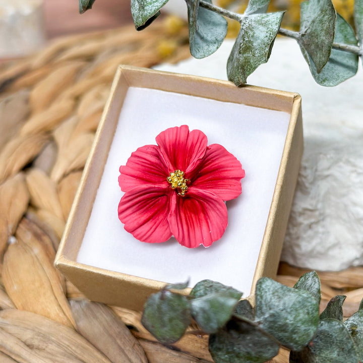 Isadora flower ring from The Dappled Wood displayed in a small gift box. Pink sculpted flower with gold center details styled with greenery on a woven background.