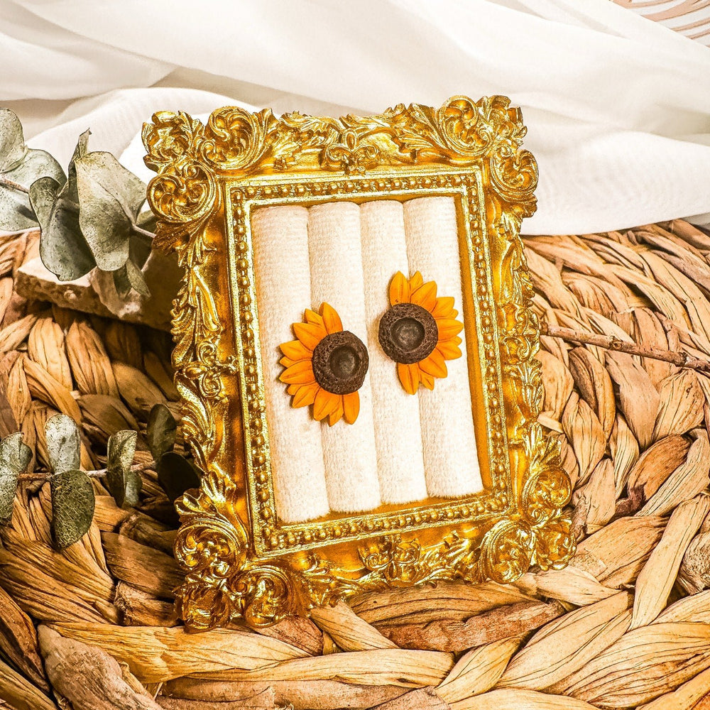 Jean half sunflower earrings with golden yellow petals and textured dark centers displayed in a gold frame