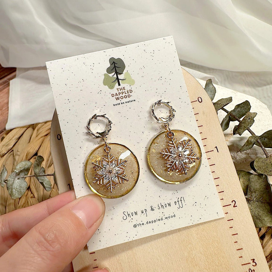 Bright product photograph of champagne snowflake resin disc earrings with fine gold edging and twig-textured hoops