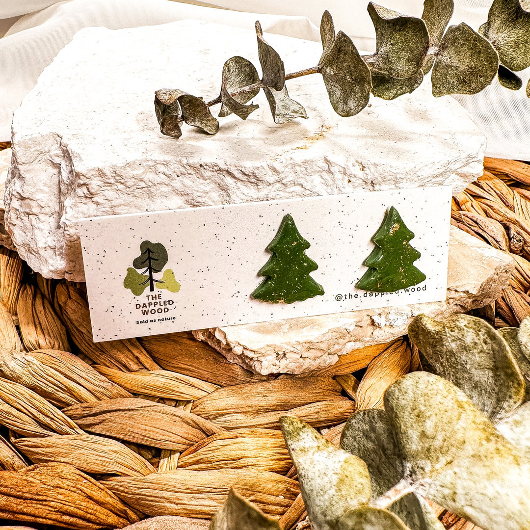 Green Christmas tree stud earrings with gold-toned flecks on a speckled jewelry card.