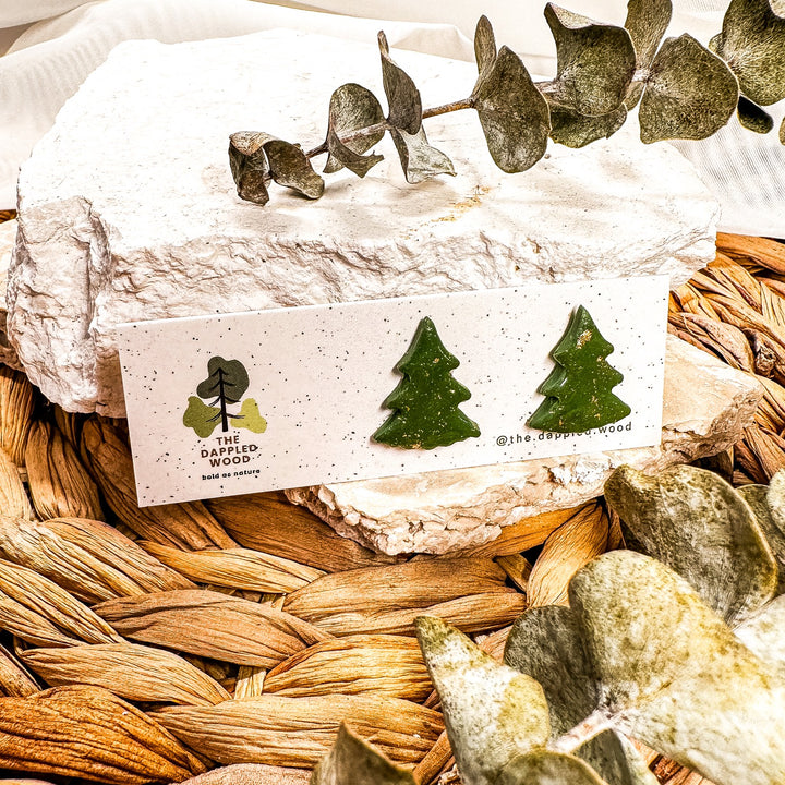 Green Christmas tree stud earrings with gold-toned flecks on a speckled jewelry card.