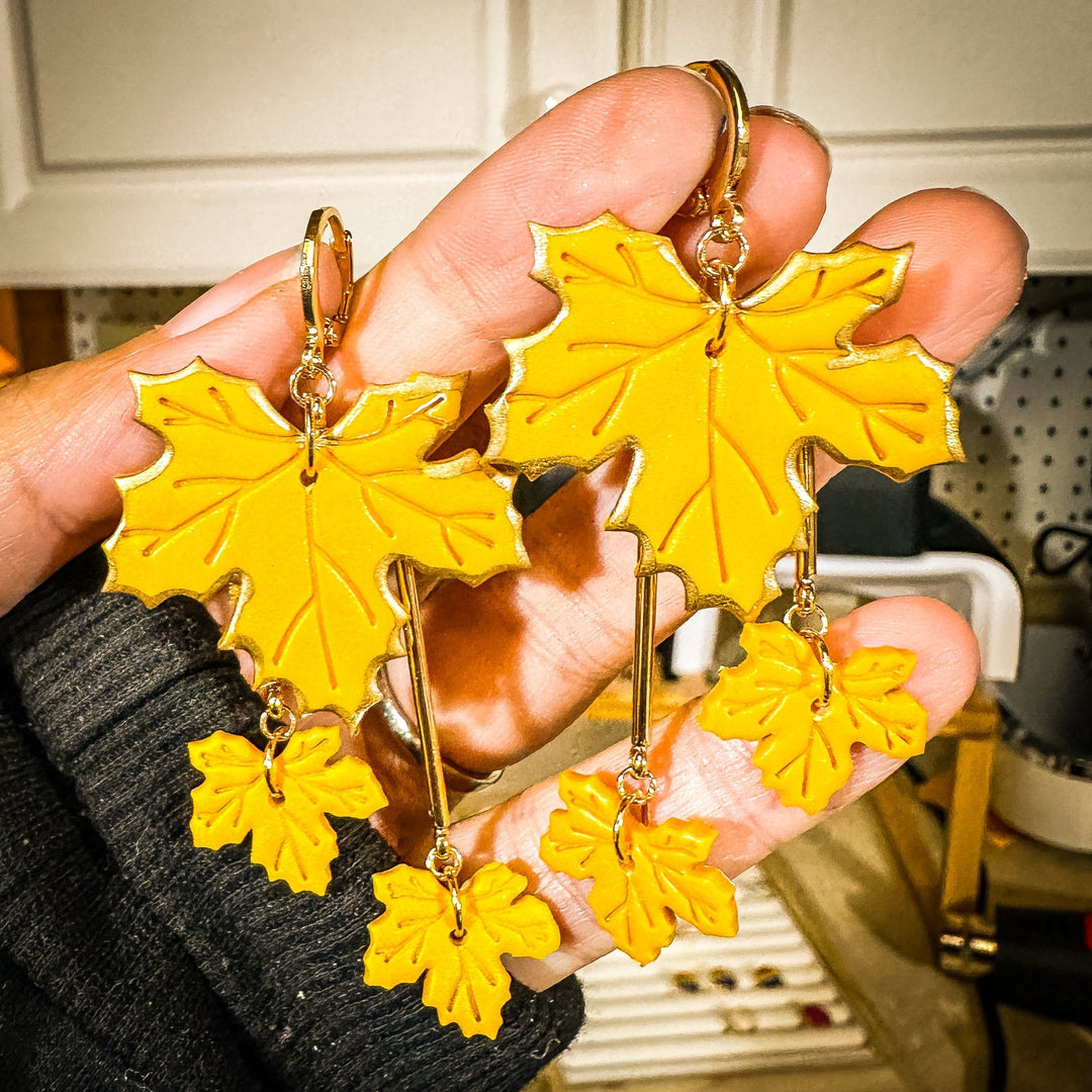 Golden yellow Laurel tiered maple leaf earrings held in a hand to show scale and detail.
