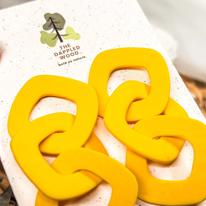 Close-up of bright yellow Lexa XL chain link statement earrings on a branded product card