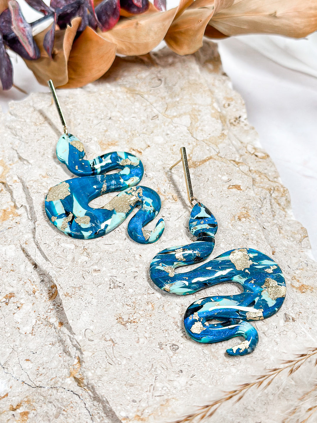 The Dappled Wood Lilith Collection snake earrings in Spooky Skies. Deep blue and black swirl polymer clay earrings with gold accents, inspired by stormy autumn nights.