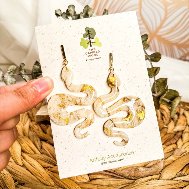 Lilith Ivory Coast cream and gold faux-stone snake statement earrings on a The Dappled Wood display card.