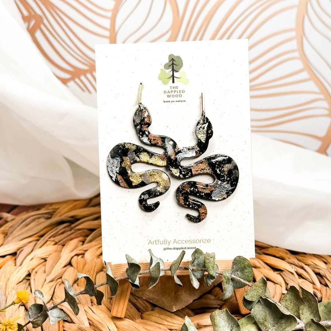The Dappled Wood's black snake earrings with gold, silver and copper metal flakes and gold bar posts.
