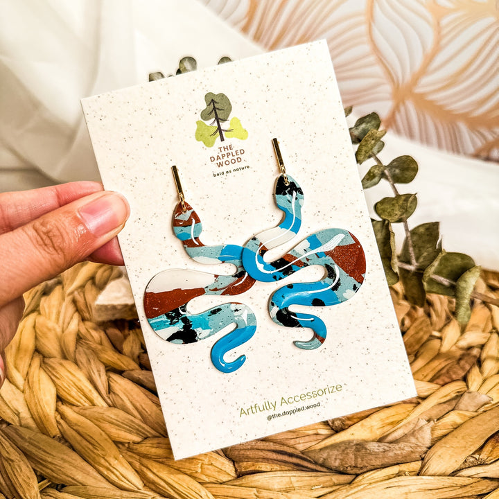 Lilith Turquoise and Terracotta snake earrings in turquoise, white, copper and black displayed on a product card.