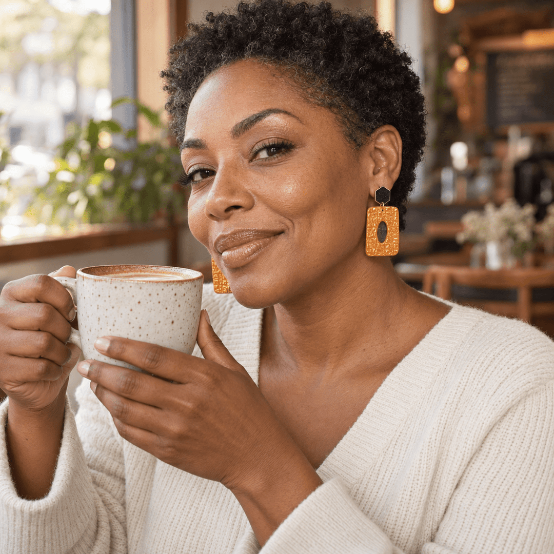 Woman enjoying coffee while wearing pumpkin orange Luella alligator-textured earrings.