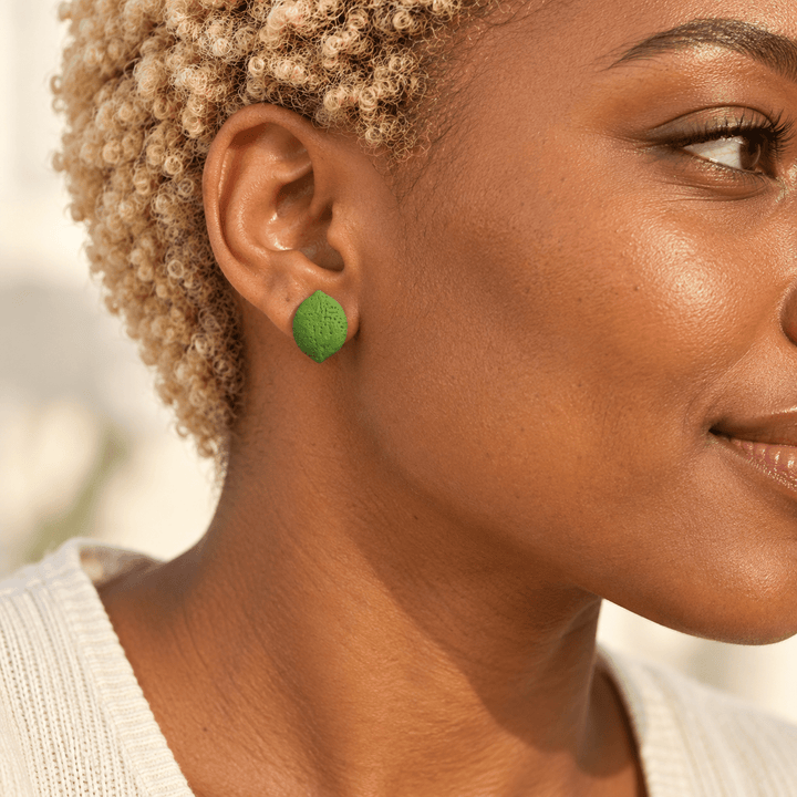 AI-generated styling preview of a model with short blonde coils wearing a Lula lime stud; scale is illustrative