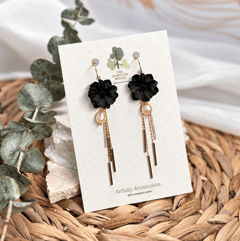 Black Maritza pearl flower earrings with long gold tassels displayed on a branded card.
