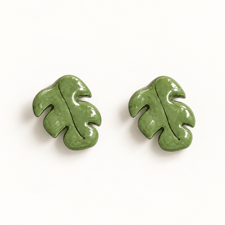 Marnie glossy olive green Monstera leaf stud earrings with carved veins on a warm white background.