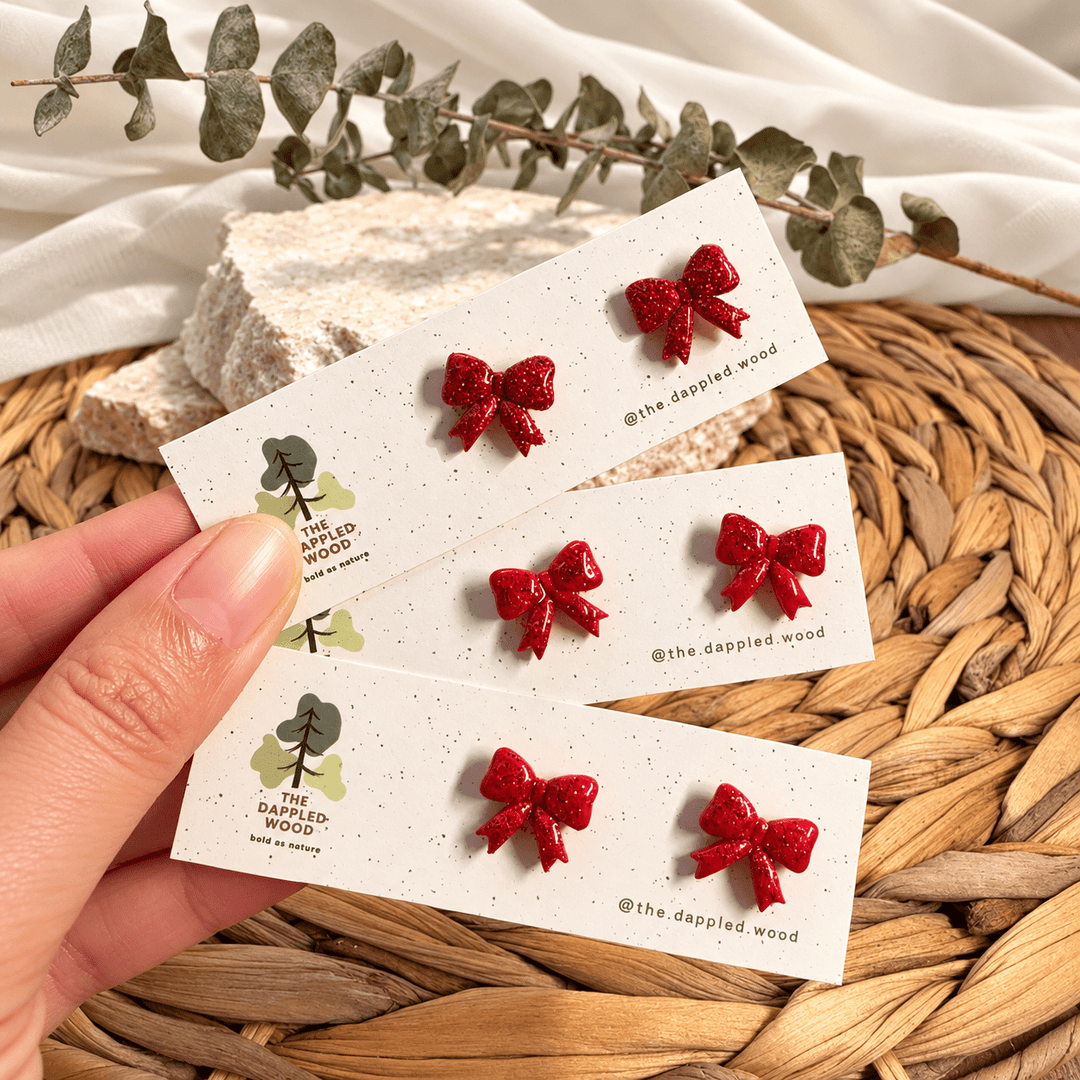 Nellie red glitter bow stud earrings displayed on cards.