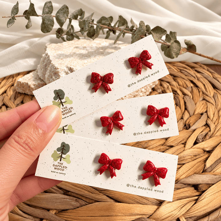 Nellie red glitter bow stud earrings displayed on cards.