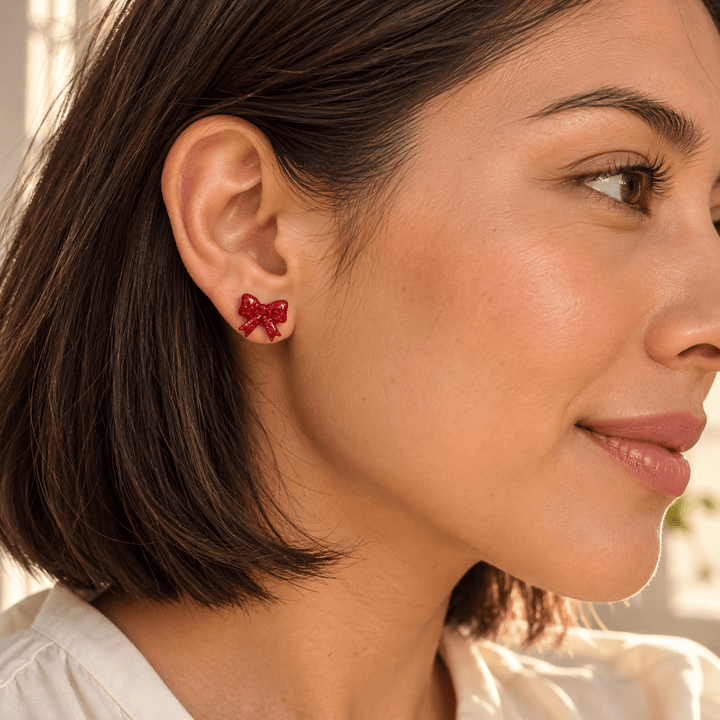 AI-generated styling preview of Nellie red bow studs on a model with olive skin and a dark bob; scale illustrative.