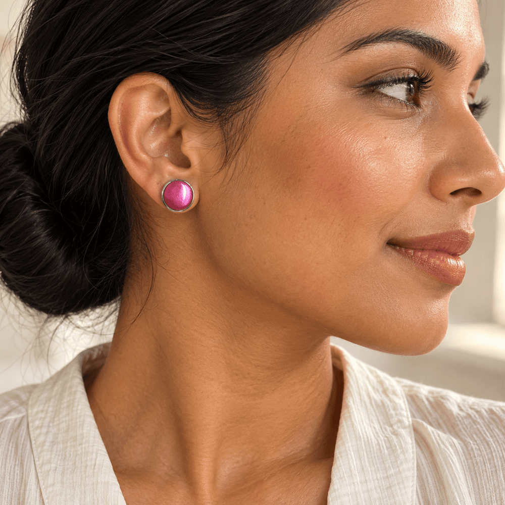 AI-generated styling preview of Nerine fuchsia silver-bezel stud earrings on a model with brown skin and a low bun; scale illustrative.