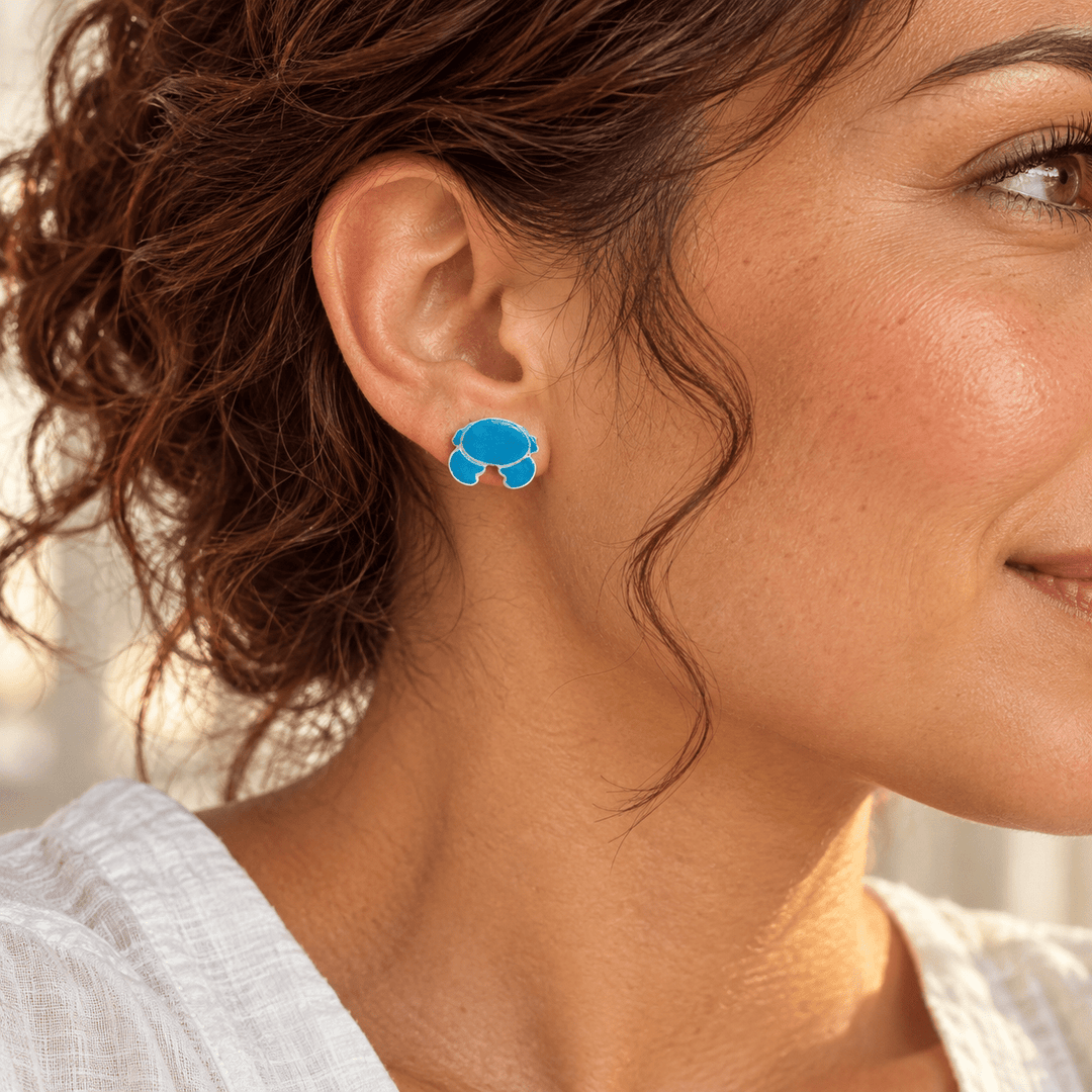 AI-generated styling preview of Nerissa blue crab stud earrings on a model with tan skin and auburn curls; scale illustrative.