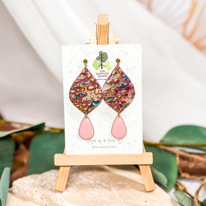 The Dappled Wood Dorothy floral teardrop earrings with shimmering gold details, displayed on an easel. Perfect for New Year's celebrations and nature-inspired statement jewelry lovers.