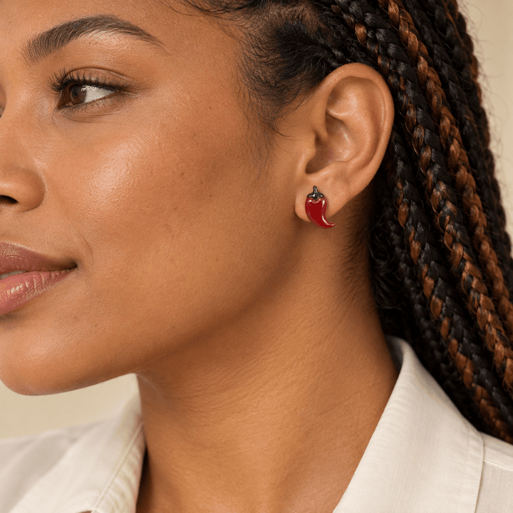 AI-generated styling preview of Pilar brick red chili pepper stud earrings on a model with copper-highlighted braids; scale illustrative.