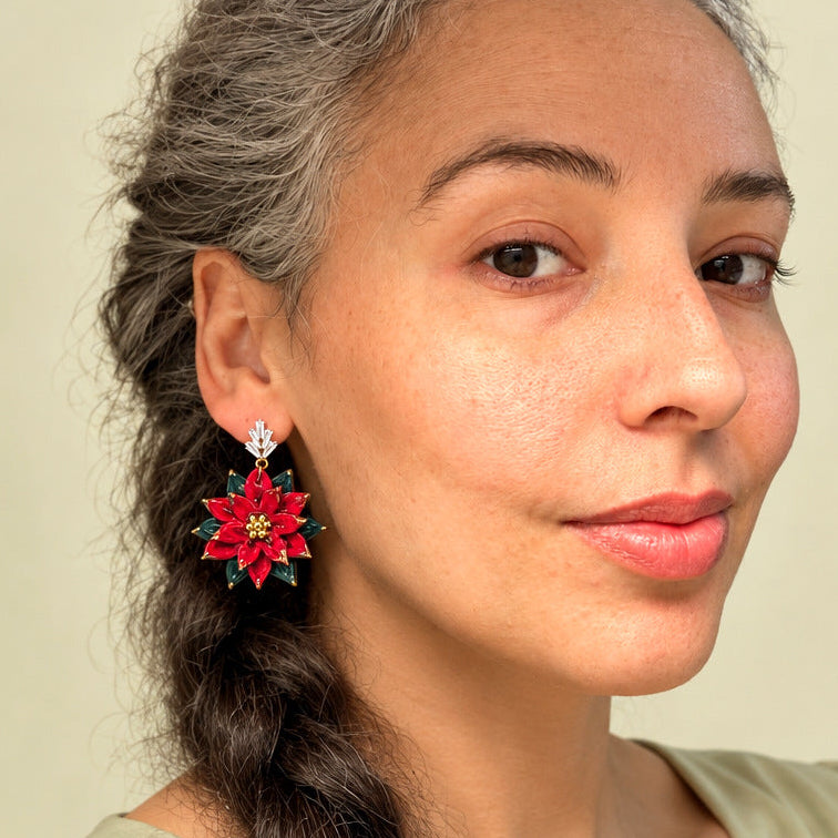 Warm studio model portrait wearing sculpted red poinsettia floral earring with green leaves and crystal stud