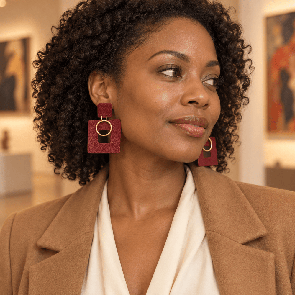 The Dappled Wood Ramona Garnet Red square earrings worn by a model in a camel jacket, showing their size and gold rings.
