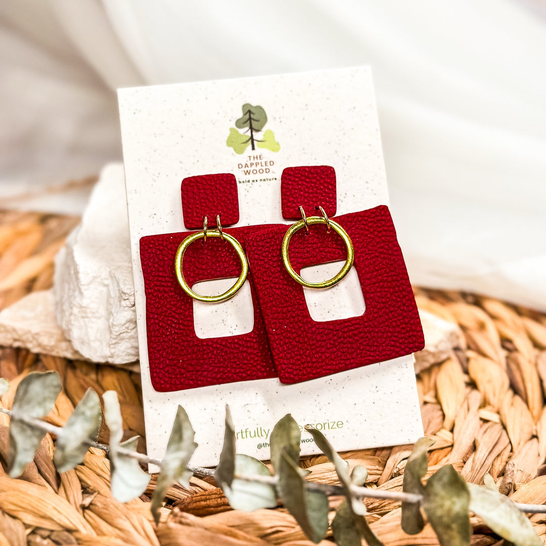 The Dappled Wood Ramona Garnet Red faux leather square earrings with gold rings on a branded product card.