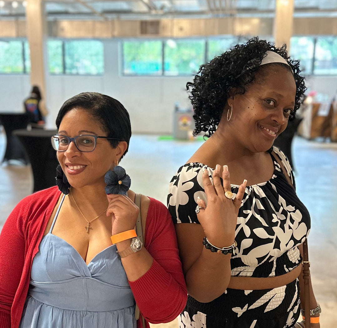 Two customers wearing Sabine earrings in Midnight and the Vivienne ring in Ivory by The Dappled Wood, showcasing bold statement jewelry in a bright indoor market setting.