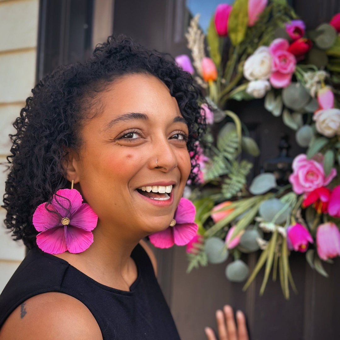 Sabine Earrings in Orchid from The Dappled Wood being worn by a smiling customer in a bright floral setting.