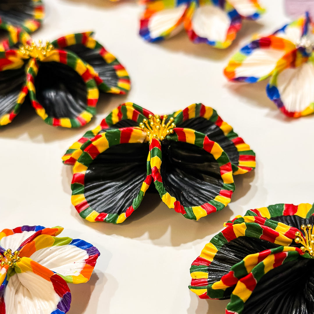 Close up of the Sade earrings by The Dappled Wood for Black History Month, featuring bold black petals with vibrant red, yellow, and green accents and gold floral detailing.