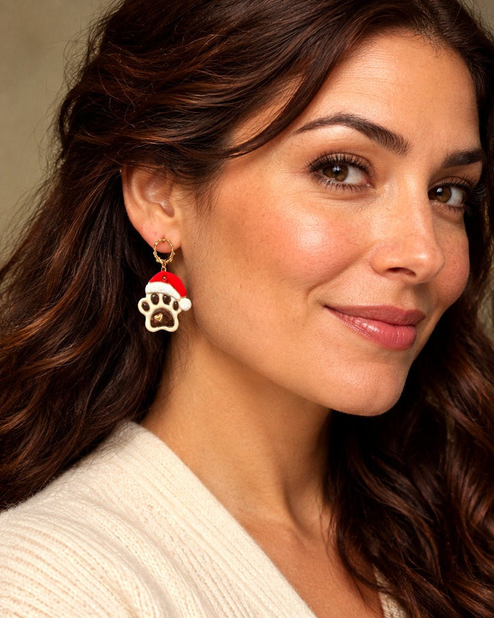 Model wearing festive Santa Paws dangle earring shaped like a paw print with red Santa hat and gold hoop