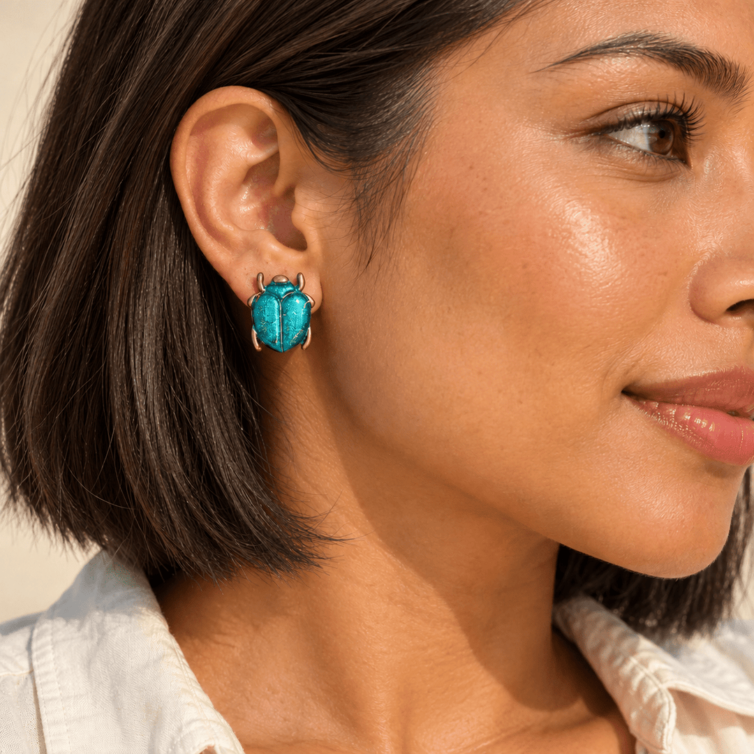 AI-generated styling preview of Caribbean Blue Saskia scarab studs on a model with a natural chestnut brown bob; scale illustrative.