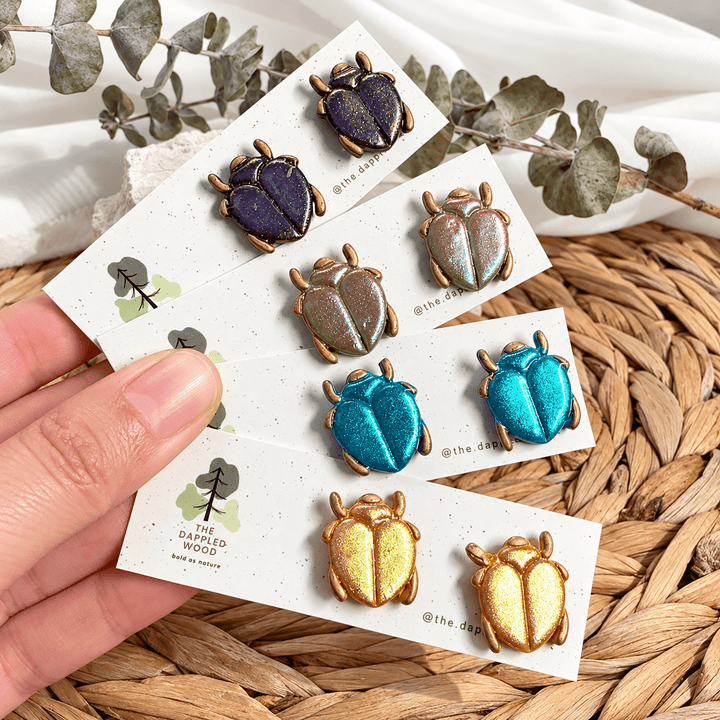 Four colorways of handmade Saskia iridescent scarab beetle studs on display cards