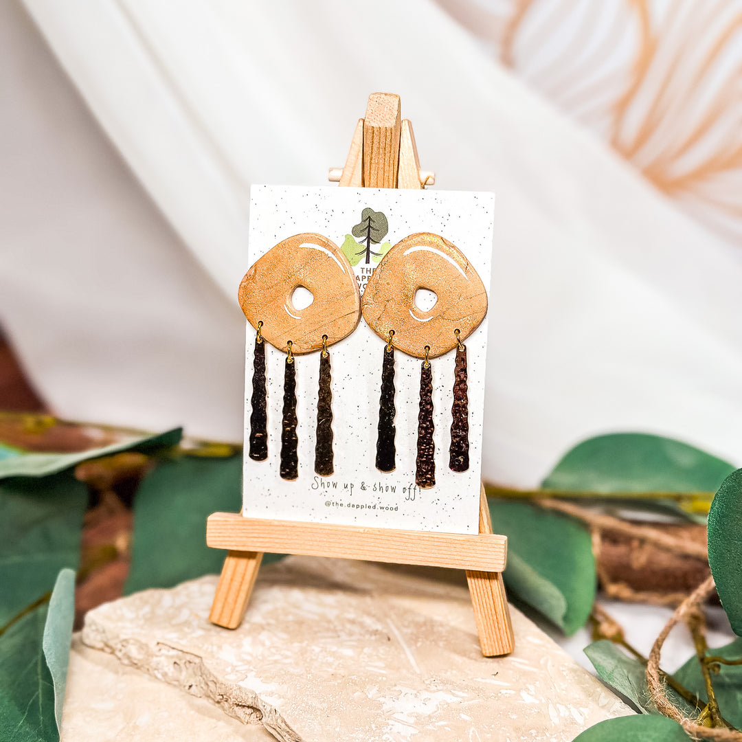 The Dappled Wood Oakley one-of-a-kind earrings from the Spring 2024 collection featuring a dappled rose gold charms from an abstract donut peach polymer clay design, suitable for sensitive ears.