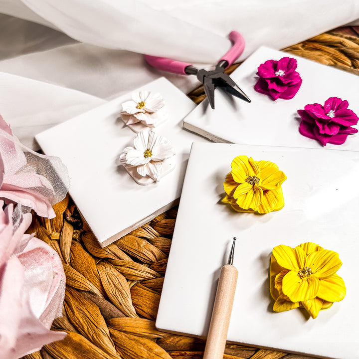 A close up of a collection of spring flower earrings and clay tools for promoting the The Dappled Wood's Flora & Flow earrings workshop and watercolor class.