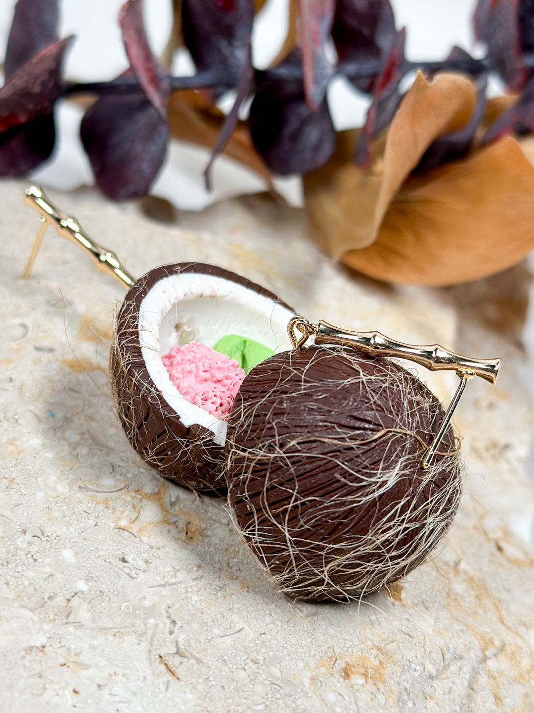 The Dappled Wood's Devi earring, which are coconuts with a pink flower and monstera leaf inside, on gold bamboo posts. Hypoallergenic for sensitive ears.